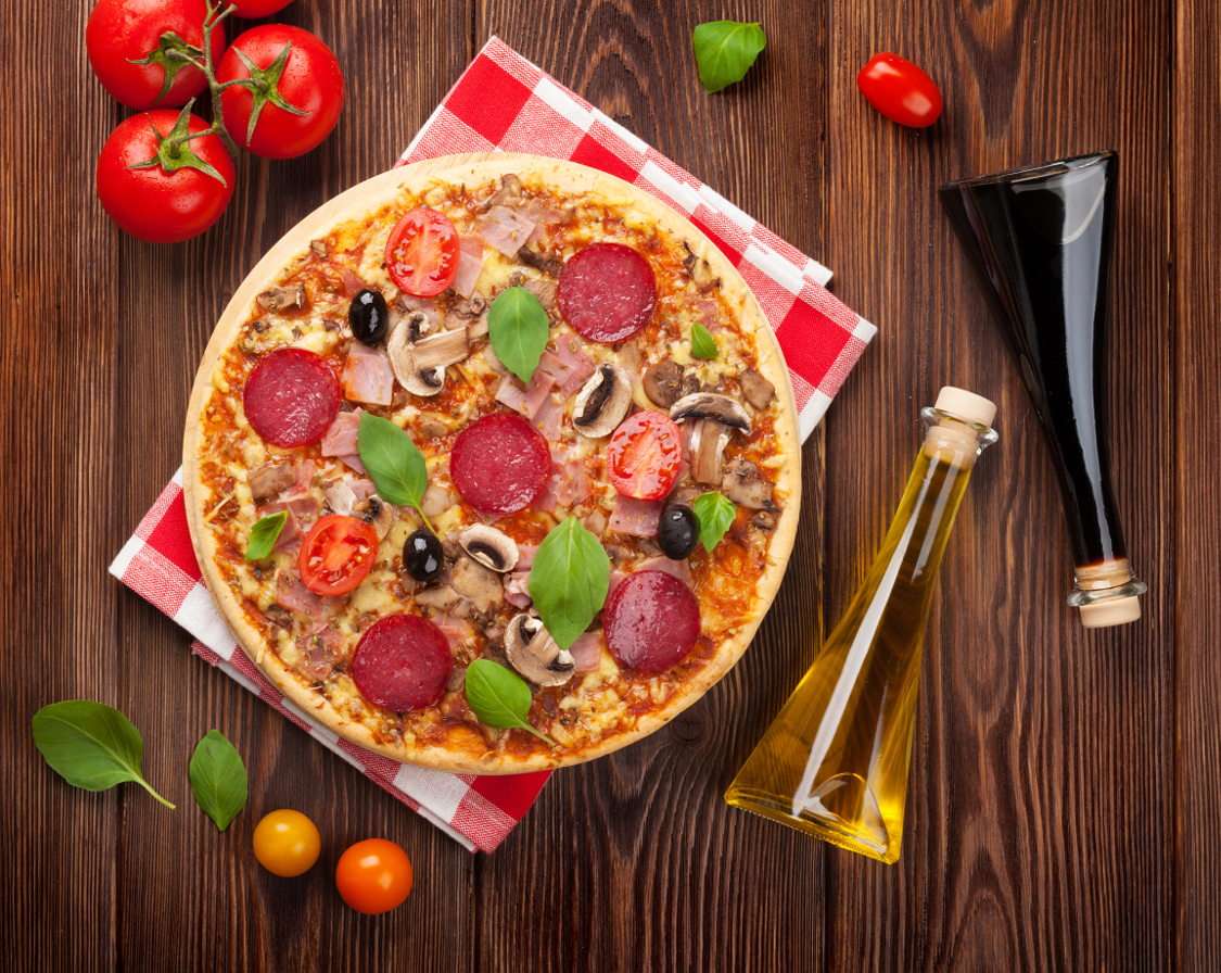 Pizza z salami, bazylią i oliwkami na drewnianym stole puzzle ze zdjęcia